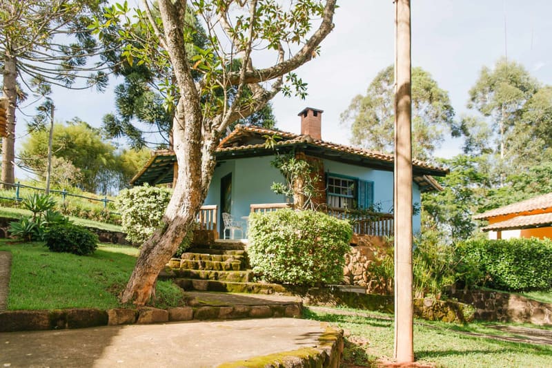 Chalé azul com escadaria de pedra cercado por jardins
